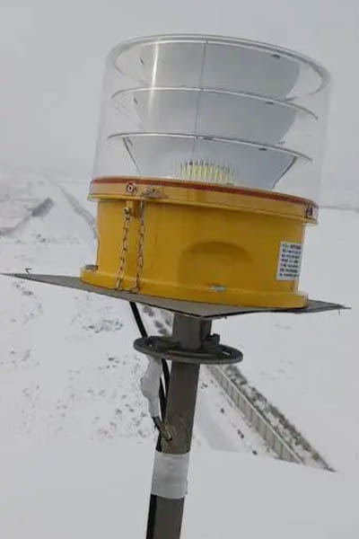 Yellow warning beacon with a clear dome mounted on a metal post in a snowy outdoor setting