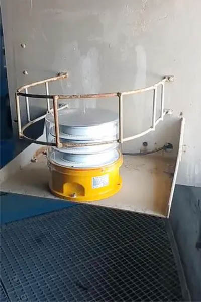 Industrial beacon light mounted on a yellow base on a metal platform with a railing in a dimly lit room