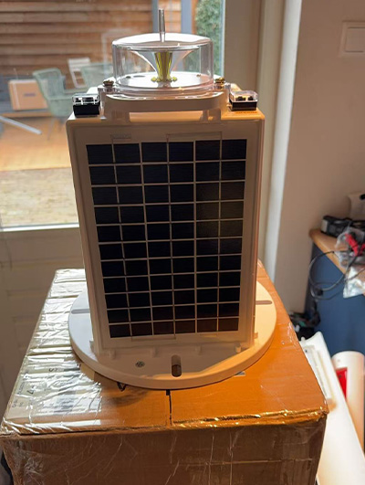 solar powered marine light YFFY Lights Small solar powered device with a rectangular solar panel on the front and a round base a turbine like fan on top placed on a cardboard box indoors near a window