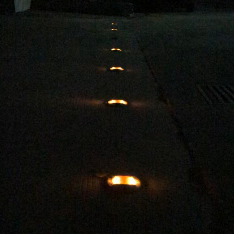Embedded Aluminum Solar Road Stud SRSA6 YFFY Lights Night scene of a sidewalk with small glowing orange path lights along the edge in darkness guiding a walkway at night