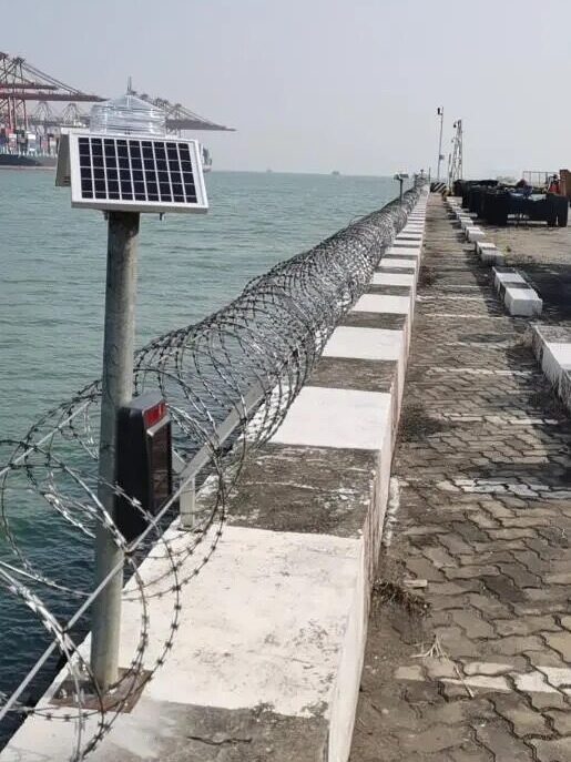 Port Solar Navigation Light Project2 YFFY Lights Harbor seawall with a barbed wire fence and a solar powered sensor on a post