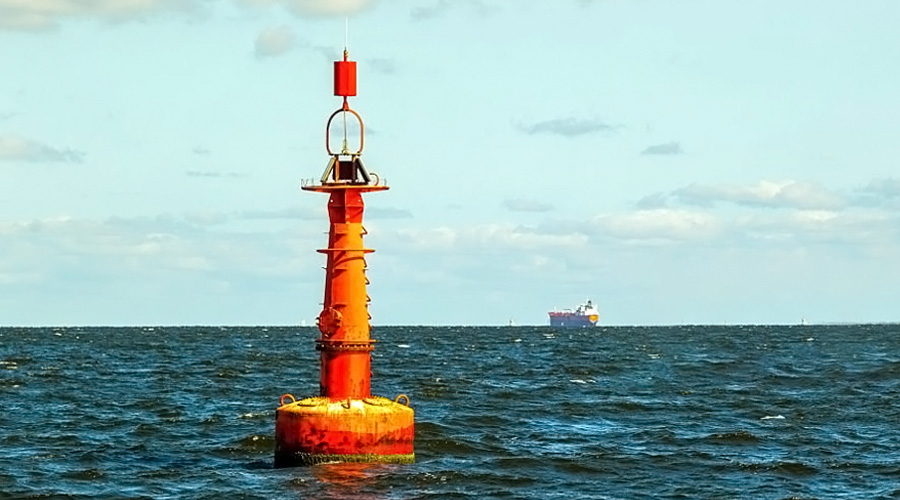 Orange offshore navigation buoy floating in choppy sea with a distant cargo ship on the horizon