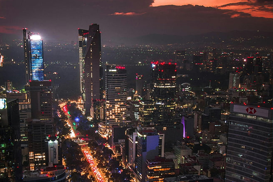 Night aerial view of a downtown skyline at dusk with tall, illuminated skyscrapers and busy neon-lit streets below.