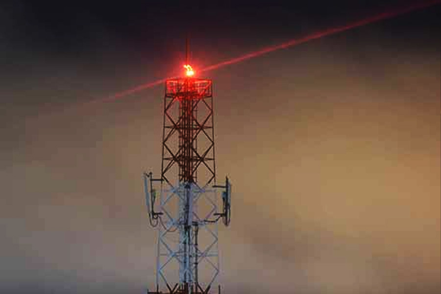 Lattice style telecommunications tower with a red beacon at the top against a dusky orange sky