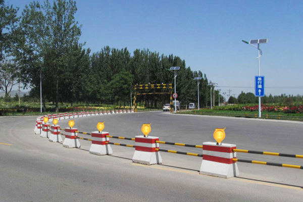 Application of Solar Barricade Warning Light Solar Warning Lights 3 YFFY Lights Road construction barriers line a curved street with orange and white blocks and amber warning lights under a clear blue sky with trees in the background