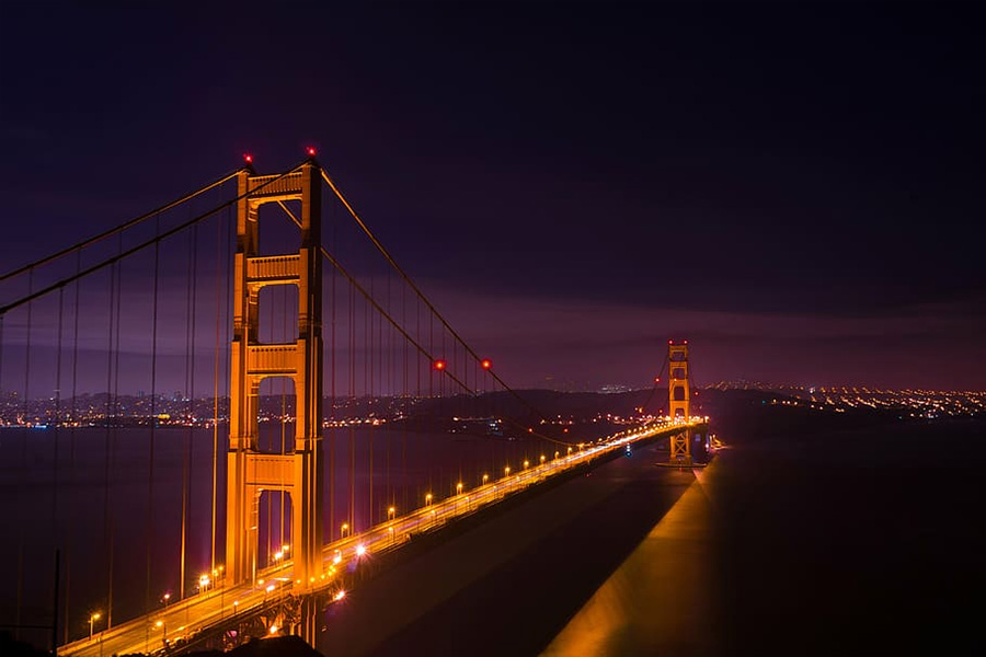 Golden Gate Bridge at night illuminated in orange lights spanning a calm bay with city lights in the background