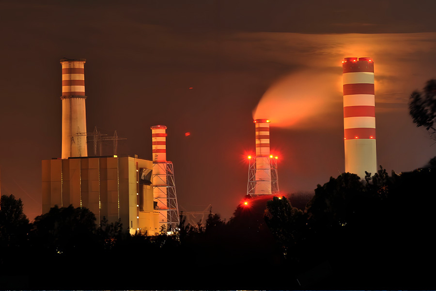 Night view of a power plant with tall red and white striped smokestacks glowing in the dark
