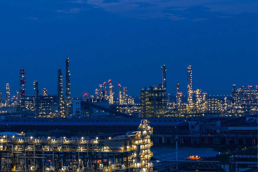 Night-time view of a large oil refinery with illuminated towers, pipelines, and machinery against a dark blue sky