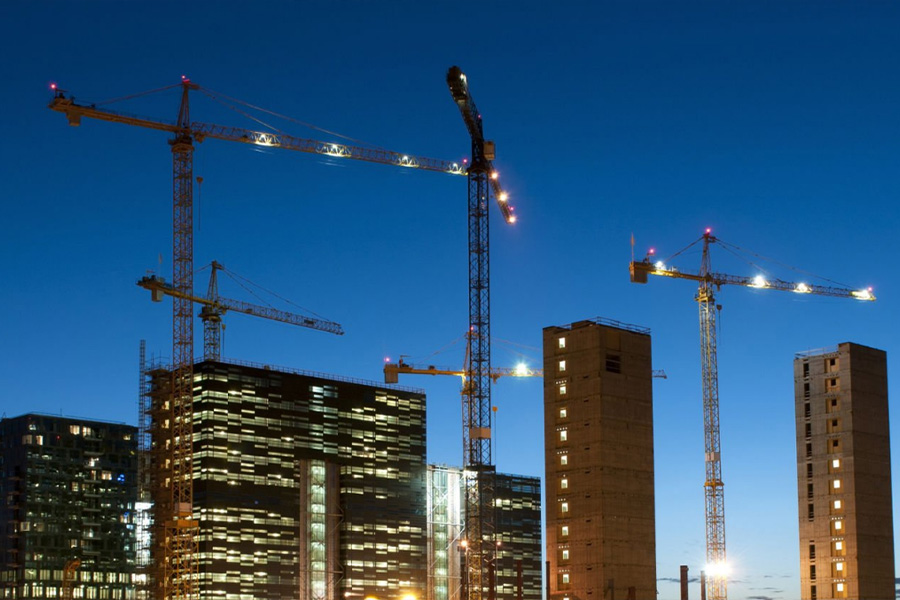 Construction site with multiple cranes over high rise buildings at dusk city lights beginning to glow in the blue sky