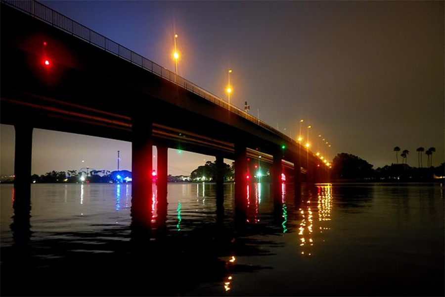 Night view of a lit bridge over calm water at dusk with reflections of streetlights on the surface