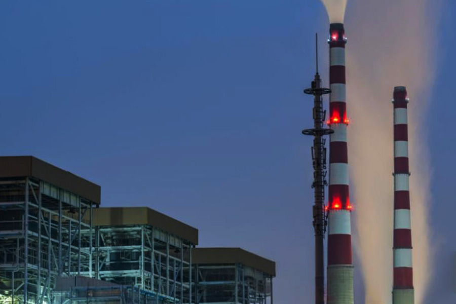 Industrial power plant with two tall red and white smokestacks emitting steam at dusk next to a metal framed facility