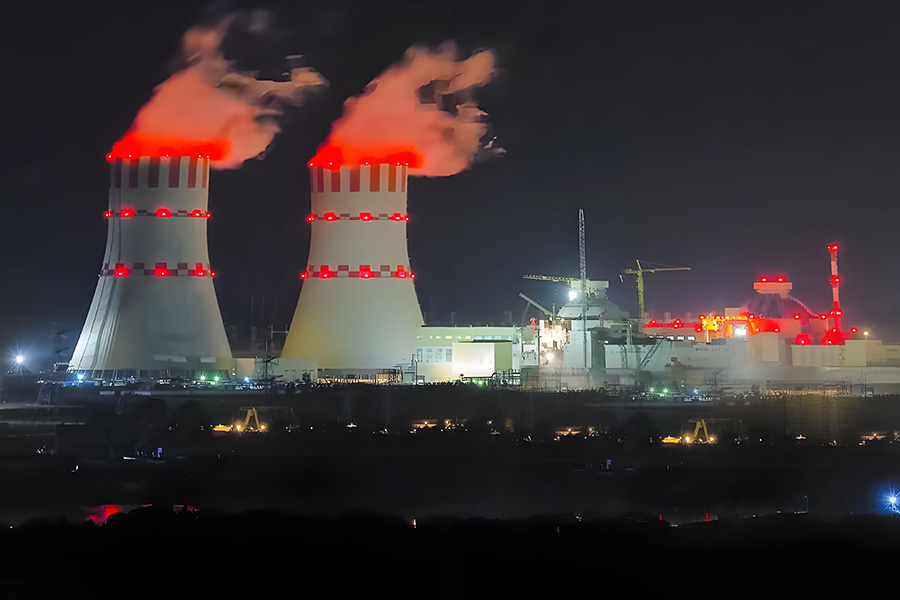 Night view of a power plant with two cooling towers emitting steam and red warning lights on the towers at night