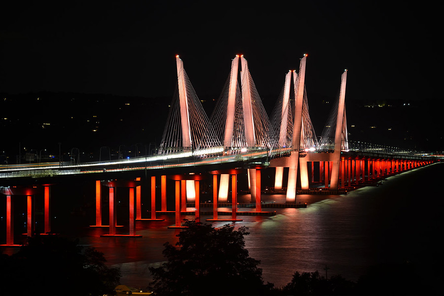 Cable stayed bridge lit in red at night with tall pylons and suspension cables spanning a dark river