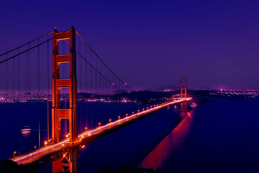 Nighttime view of the Golden Gate Bridge in San Francisco lit orange with city lights along the shoreline