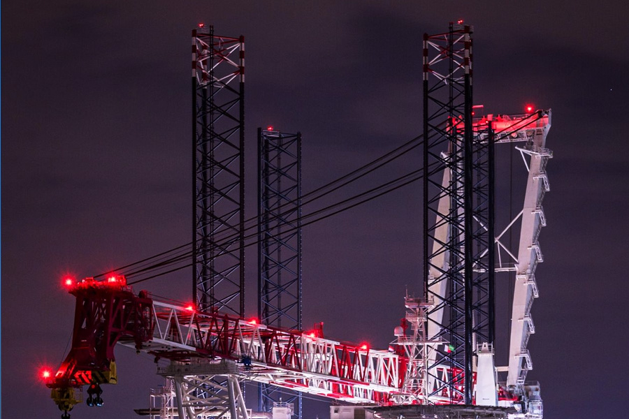 Night scene of a large construction crane with red aviation lights and tall lattice towers at night.