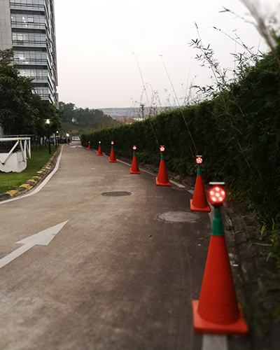 Road under lane closure with orange traffic cones and blinking lights along a hedge on the right building to the left Inset white arrow on pavement